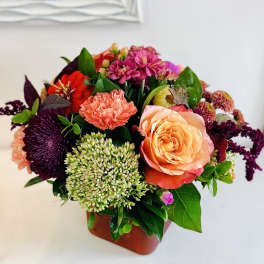 Mixed bouquet with peach rose, coral carnation, and purple blooms in a vase