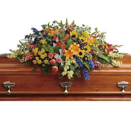 Large multicolored casket spray of lilies, roses, and mixed flowers on a wooden coffin