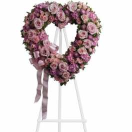 Heart-shaped pink rose wreath on a white stand with ribbon