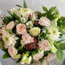 Hand-tied bouquet of white mums, pale pink carnations, and pastel roses with greenery