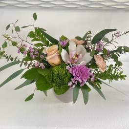 Mixed floral arrangement in a white vase with roses, orchids, and purple blooms