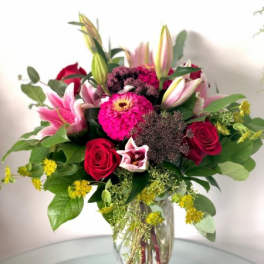 Clear vase arrangement with pink lilies, bright pink blooms, and red roses