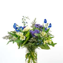 Mixed bouquet of blue, purple, and cream flowers in a clear glass jar vase