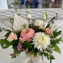 Pink roses, peach carnations, and white blooms in a glass cube vase with ribbon.