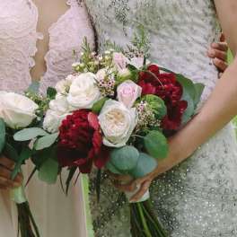 Two women hold bridal bouquets of white, pink, and deep red flowers.