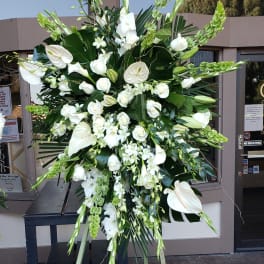 Large white funeral spray on a stand with lilies, roses, and orchids