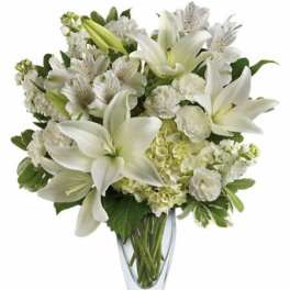 White lilies and mixed white flowers in a clear glass vase