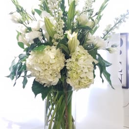 White floral arrangement in a tall glass vase with lilies and hydrangeas