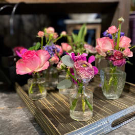 Small pink and purple floral arrangements in clear glass bottles on a tray