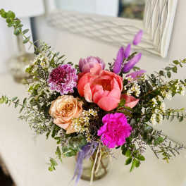 Mixed arrangement of pink peonies, roses, and carnations in a clear glass vase