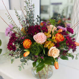 Vibrant arrangement of pink and peach roses, orange tulips, and burgundy mums in a clear glass vase