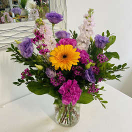 Mixed bouquet of yellow, pink, and purple flowers arranged in a clear glass vase.