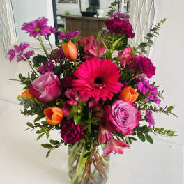 Bright mixed bouquet in a clear glass vase with pink, orange, and purple flowers
