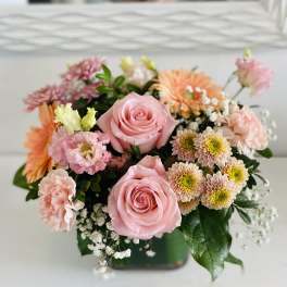Pink roses and mixed pastel flowers arranged in a low square vase