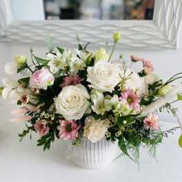 Low white ceramic vase filled with white roses, pink daisies, and soft pastel mixed flowers.
