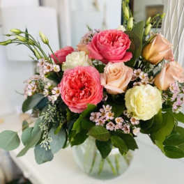 Mixed arrangement of pink and cream roses with small white blossoms in a clear glass bowl vase
