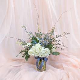 White hydrangea bouquet in a glass vase with blue accents and ribbon
