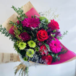 Hand-tied bouquet of red roses, bright pink gerberas and green mums wrapped in kraft and pink paper