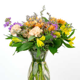 Mixed bouquet of yellow, purple, and peach flowers in a clear glass vase