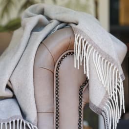 A light gray throw blanket draped over a beige upholstered chair