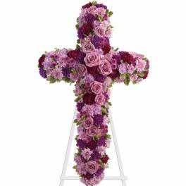 Tall floral cross of pink and purple blooms displayed on a white easel stand