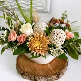 Low arrangement of peach roses, white rose, yellow chrysanthemum and white pods in a bowl vase