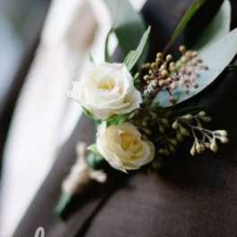 Ivory rose boutonniere with buds and greenery pinned to a dark suit lapel