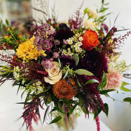 Mixed bouquet of orange, yellow, burgundy, and cream flowers in a glass vase