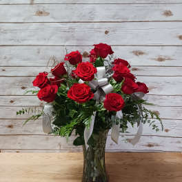 Red roses arranged in a clear glass vase with white ribbons