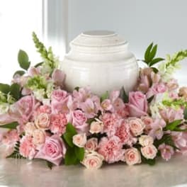 Pink roses and carnations arranged around a white urn.