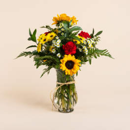 Bouquet of sunflowers, daisies, and red carnations in a glass vase