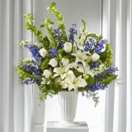 White lilies and blue flowers arranged in a white vase