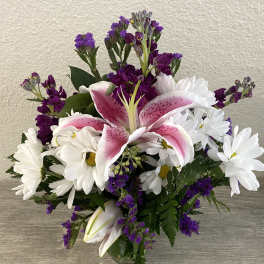 Bouquet of pink lilies and white daisies with purple filler flowers in a glass vase