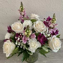 Bouquet of white roses, pink snapdragons, and white carnations in a glass vase