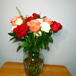Mixed red, peach, and white roses arranged in a clear glass vase on a wooden surface.