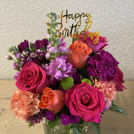 Bright mixed bouquet in a glass vase with a birthday topper