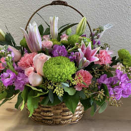 Basket arrangement with pink lilies, roses, carnations, and purple blooms