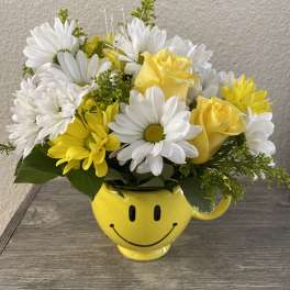 Yellow and white flowers arranged in a smiley-face mug