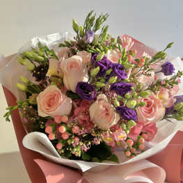 Bouquet of pink and purple roses with mixed blooms wrapped in pink paper