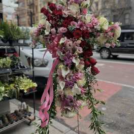 Tall floral standing spray with red, pink, and white blooms and a pink ribbon