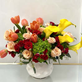 Bouquet of red and peach roses with orange tulips and yellow calla lilies in a white vase