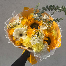 Bouquet of sunflowers, yellow roses, and white daisies wrapped in orange paper