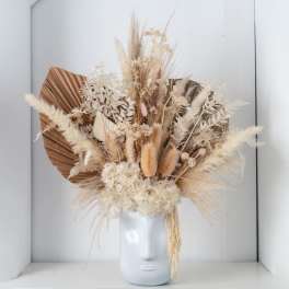 Neutral dried flower arrangement with hydrangea and grasses in a white ceramic face-shaped vase