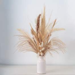 Tall arrangement of dried beige grasses and seed heads in a simple white ceramic vase