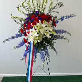 Standing floral tribute with white lilies, red carnations, and blue flowers on a metal easel