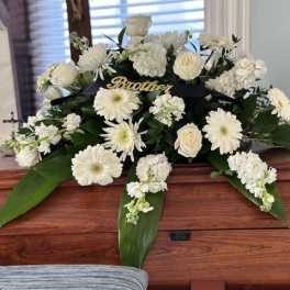 White funeral spray on a wooden casket with a black ribbon