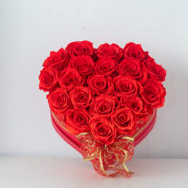 Heart-shaped box filled with red roses and tied with a red and gold ribbon bow.