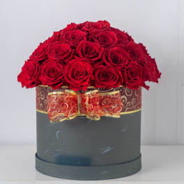 Round hat box filled with red roses, wrapped with a red and gold ribbon and bow