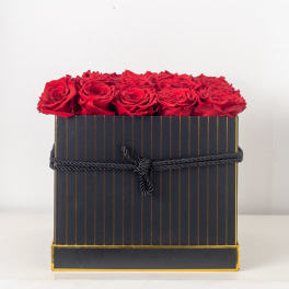 Square black striped box filled with tightly packed red roses