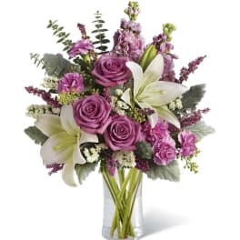 Purple roses and white lilies in a clear glass vase